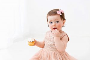 a one year old girl in sequin peach dress holding a cupcake