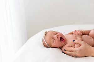 newborn baby yawning wearing a white headband laying on a newborn photography bean bag